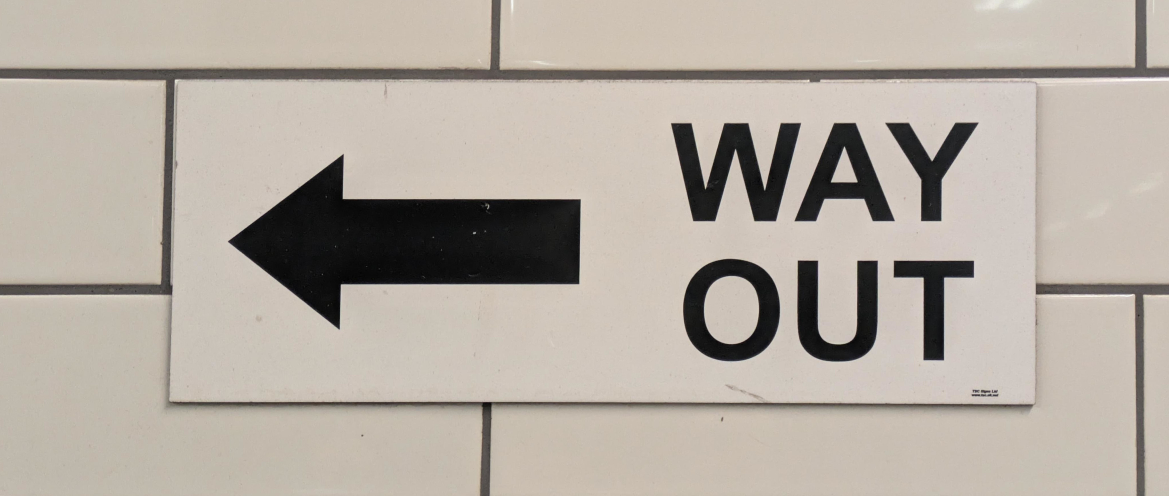 A sign Way Out with an arrow to the left on a tiled wall