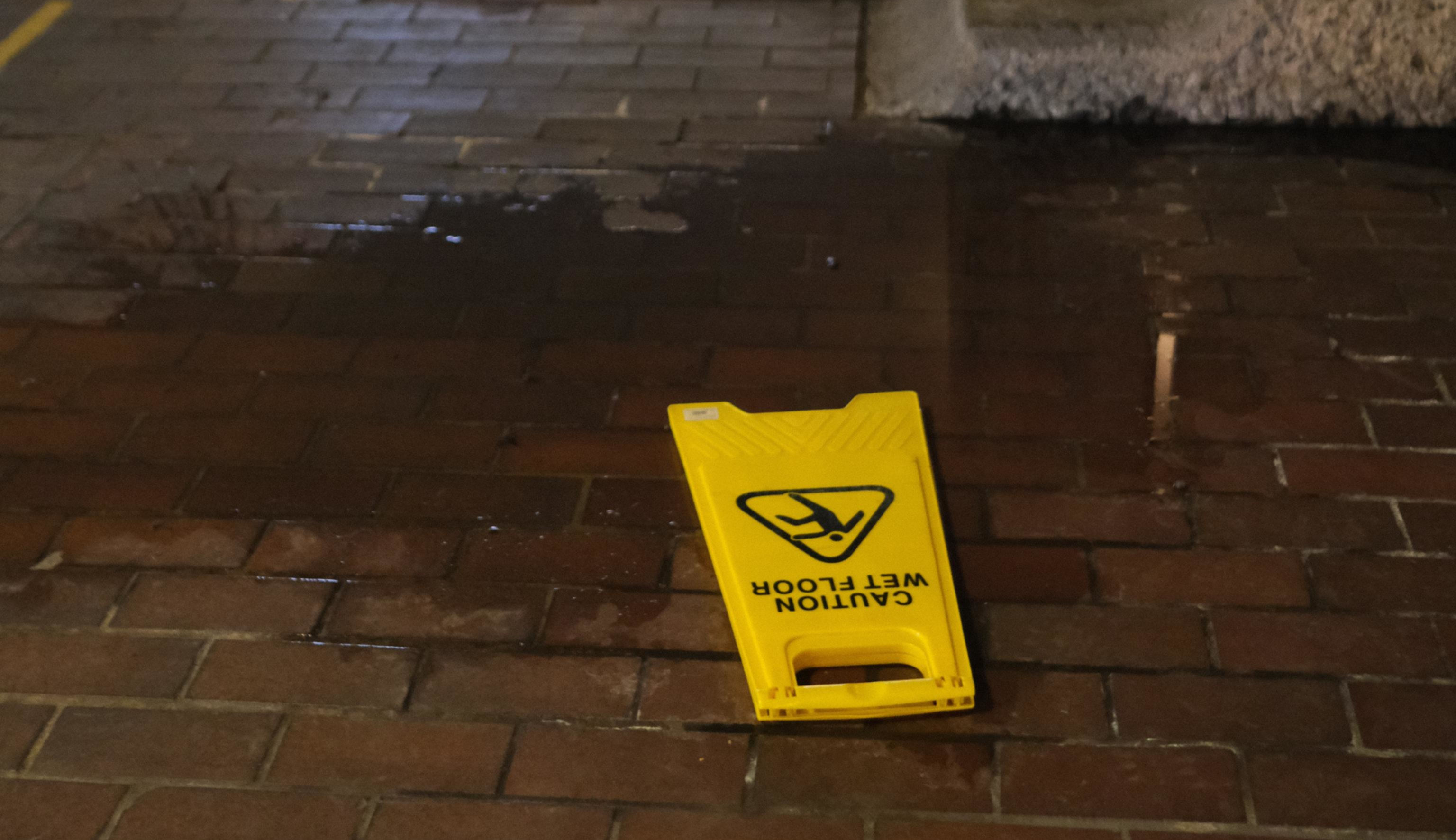 A wet floor sign lying in a puddle on a brick floor